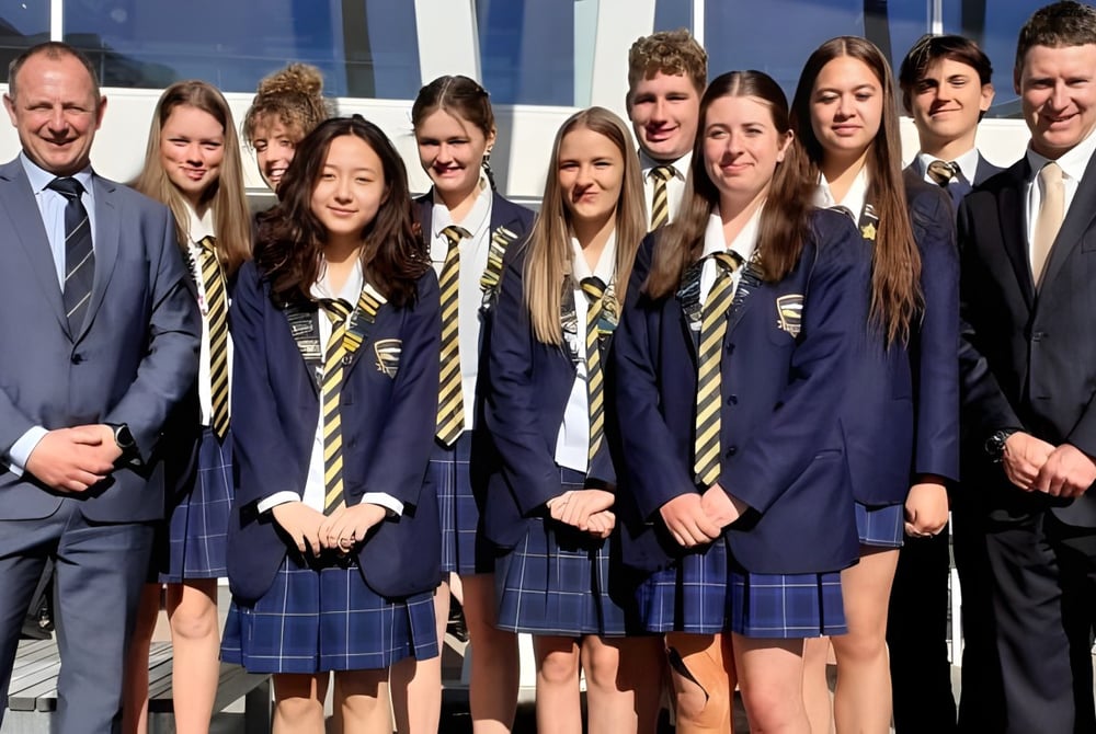 Eine Gruppe Schülerinnen und Schüler der Wakatipu High School posiert vor einem modernen Gebäude mit großen Fenstern.