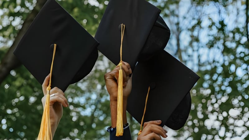 Zwei schwarze Abschlussmützen mit goldenen Quasten werden auf dem Campus des Walkerville Collegiate Institute hochgehalten.