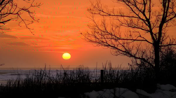 Ein oranger Sonnenuntergang beleuchtet den Himmel über dem Gewässer nahe dem Walkerville Collegiate Institute.