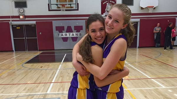Zwei Schülerinnen der Wallaceburg District High School umarmen sich und lächeln auf dem Basketballfeld vor einem Tartans-Schild.