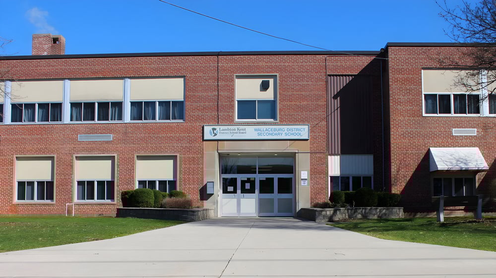 Das zweistöckige Backsteingebäude der Wallaceburg District High School mit großen Fenstern steht unter einem klaren blauen Himmel.