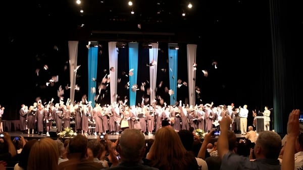 Auf der Bühne der Walnut Grove Secondary School treten zahlreiche Schülerinnen und Schüler in weißen Roben auf.