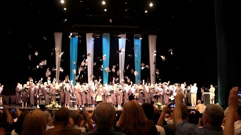Auf der Bühne der Walnut Grove Secondary School treten zahlreiche Schülerinnen und Schüler in weißen Roben auf.