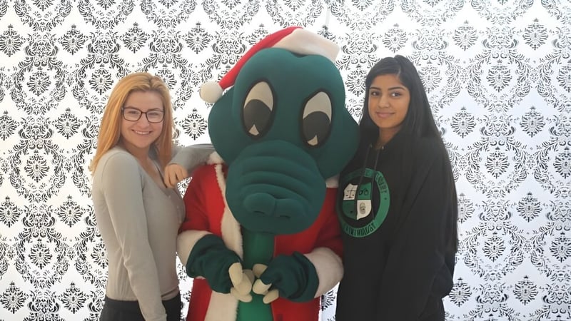 Zwei Schülerinnen posieren mit einer großen grünen Comicfigur vor gemusterter Tapete an der Walnut Grove Secondary School.