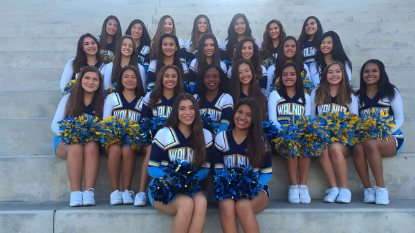 Eine Gruppe von Cheerleadern in blauen und gelben Uniformen posiert vor einer Betonwand auf dem Campus des Walnut Valley School District.