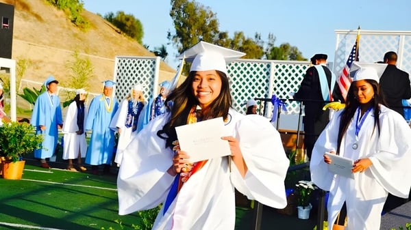 Absolventinnen und Absolventen in weißen Gewändern und Hüten stehen auf einer Wiese auf dem Gelände des Walnut Valley School District.