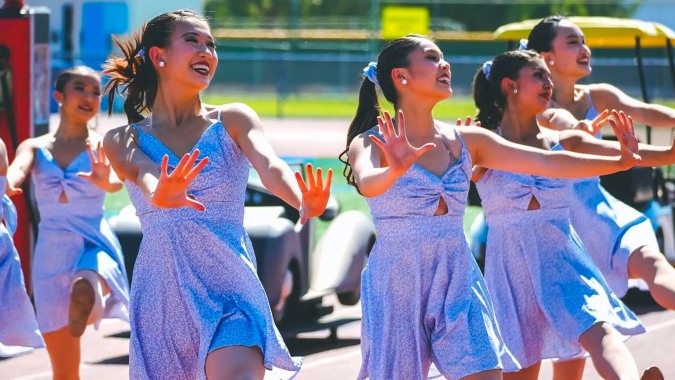 Schülerinnen des Walnut Valley School District tanzen gemeinsam in bunter Kleidung bei einer Feier im Freien.