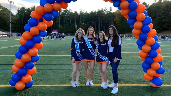 Vier Schülerinnen der Walpole High School stehen gemeinsam vor einem Ballonbogen auf dem Sportplatz.