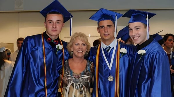 Drei Schüler in blauen Abschlusskleidern und eine Frau in buntem Kleid feiern gemeinsam die Abschlussfeier der Walpole High School.