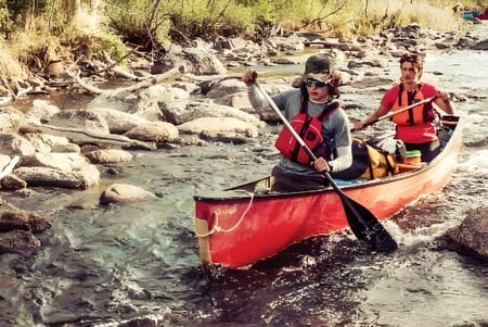 Zwei Personen fahren mit einem kleinen roten Boot auf einem seichten Fluss nahe der Walter Murray Collegiate.