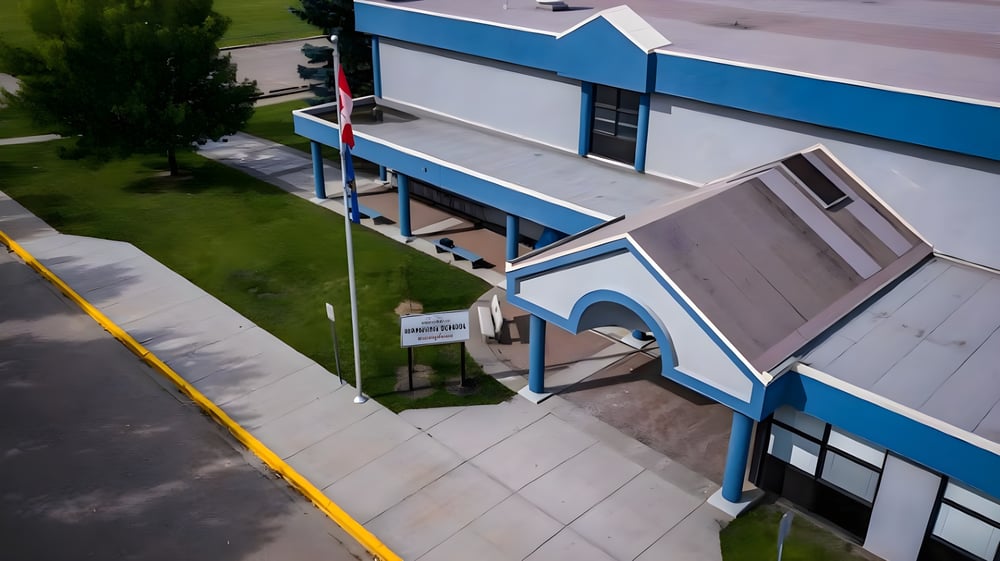 Das moderne mehrstöckige Gebäude der Warburg School mit blauer und grauer Fassade ist von einer Rasenfläche und einem gepflasterten Weg umgeben.