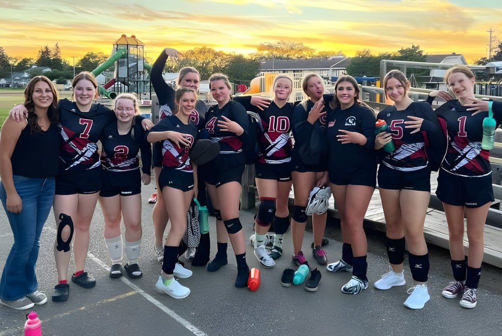 Eine Gruppe junger Sportlerinnen der Warburg School posiert gemeinsam auf dem Sportplatz vor Spielplatzgeräten.