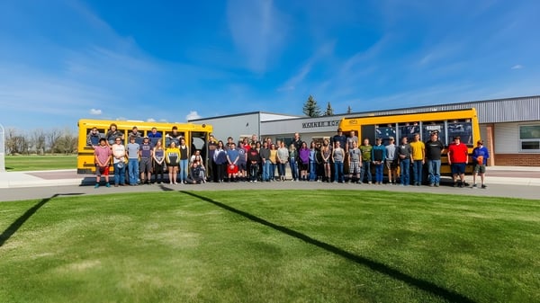 Eine Gruppe von Schülern und Erwachsenen steht vor einem gelben Schulbus auf dem Gelände der Warner School.