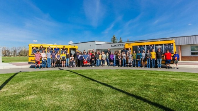 Schüler und Erwachsene stehen vor einem gelben Schulbus auf einer Wiese auf dem Gelände der Warner School.