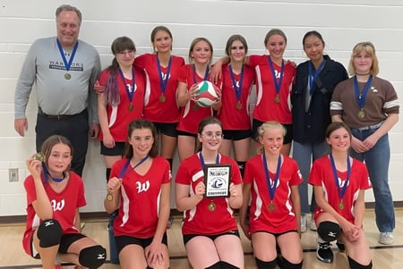 Das Volleyballteam der Warner School mit Trainerinnen posiert in der Sporthalle mit einem Pokal.