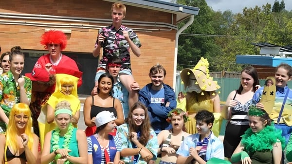 Eine Gruppe von Schülerinnen und Schülern der Warners Bay High School steht vor einem Holzgebäude in bunten Kostümen.