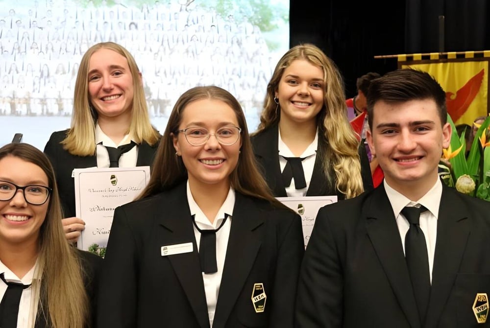 Eine Gruppe von Schülern der Warners Bay High School steht gemeinsam in formeller Kleidung vor dem Schulgebäude.