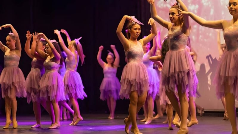 Schülerinnen führen eine Tanzaufführung in pink-lila Kostümen auf der Bühne der Warwick Senior High School auf.