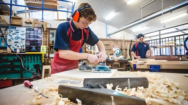 Eine Schülerin oder ein Schüler der Warwick Senior High School arbeitet mit einem Elektrowerkzeug an einem Holzprojekt in der Werkstatt.