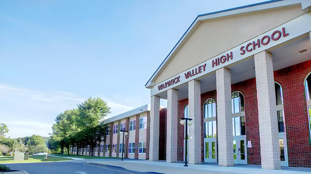 Das zweistöckige Backsteingebäude der Warwick Valley High School ist umgeben von Bäumen und einem gepflasterten Vorplatz.