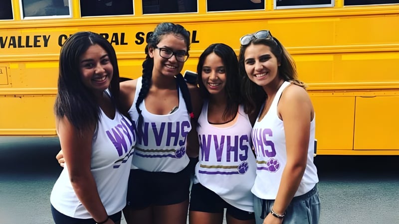 Vier Schülerinnen der Warwick Valley High School posieren vor einem gelben Schulbus.