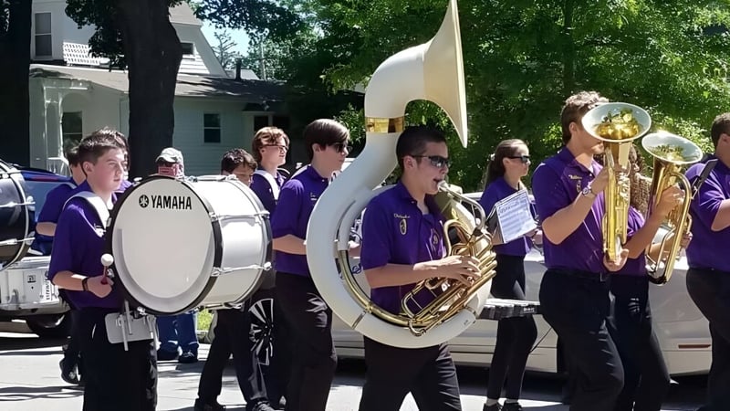 Eine Musikergruppe in lila Uniformen spielt auf der Straße vor Gebäuden auf dem Gelände der Warwick Valley High School.