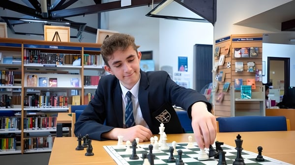 Ein Schüler der Warwick School spielt konzentriert Schach in einer von Bücherregalen umgebenen Lernumgebung.