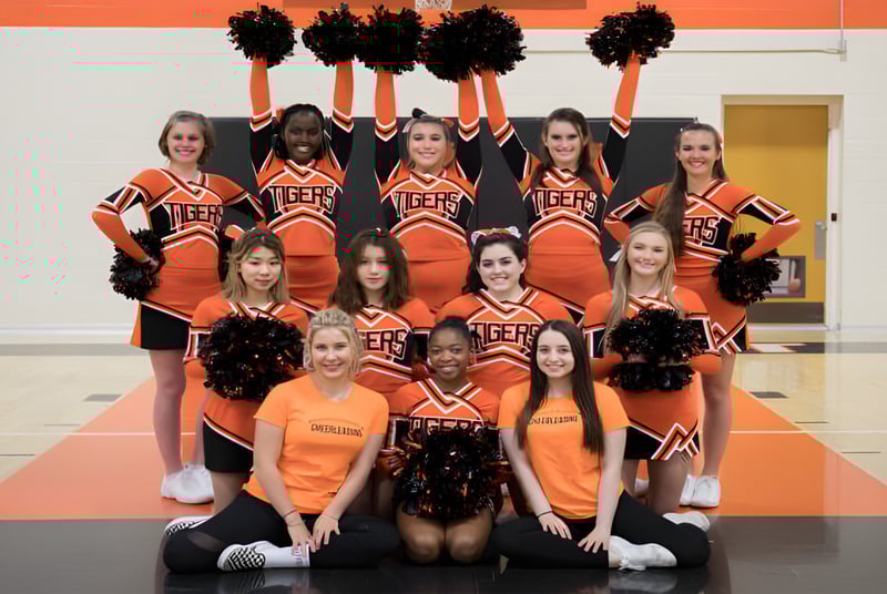 Eine Gruppe Cheerleader der Wasatch Academy posiert in orangenen und schwarzen Uniformen in der Turnhalle.
