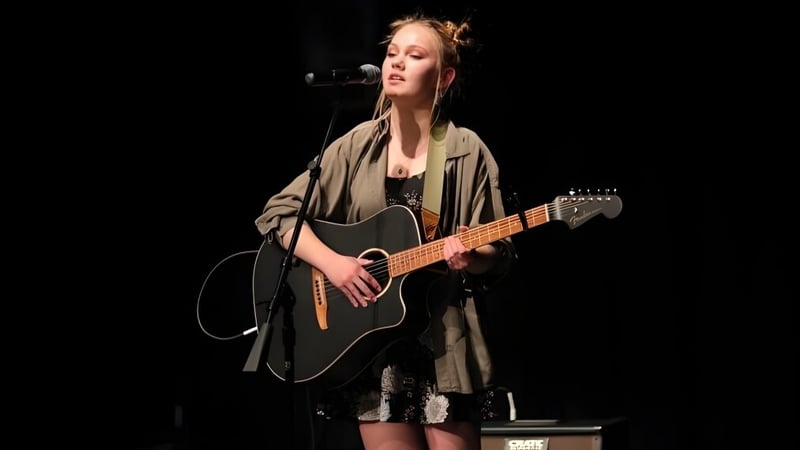 Eine Schülerin der Wasatch Academy spielt auf der Bühne Akustikgitarre und singt in ein Mikrofon.