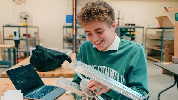 Ein Schüler der Wasatch Academy arbeitet lächelnd an einem Laptop in einer Werkstatt.