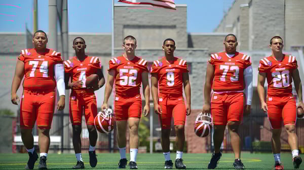 Eine Gruppe von Fußballspielerinnen und Fußballspielern der Washington Academy steht in roten Trikots auf dem Spielfeld vor einem Gebäude mit amerikanischer Flagge.