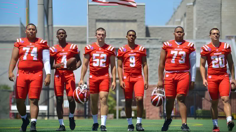 Eine Gruppe von Fußballspielerinnen und Fußballspielern der Washington Academy steht in roten Trikots auf dem Spielfeld vor einem Gebäude mit amerikanischer Flagge.
