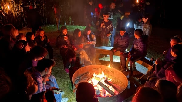 Eine Gruppe von Schülerinnen und Schülern der Washington Preparatory School sitzt im Freien um ein Lagerfeuer und unterhält sich.