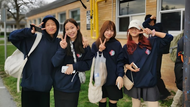 Eine Gruppe junger Schülerinnen in Schuluniformen steht vor einem gelben Gebäude auf dem Campus des Waterloo Catholic District School Board.