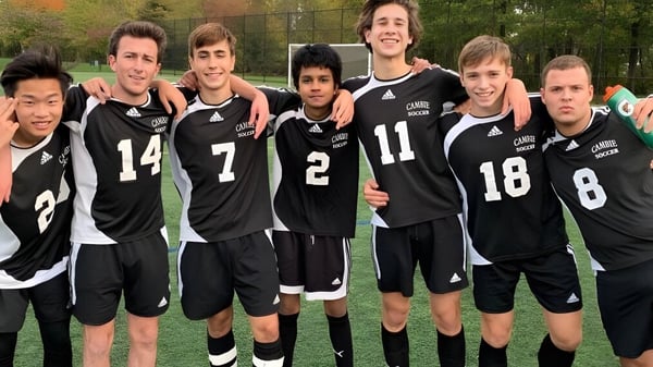 Eine Gruppe von Schülern des Waterloo Catholic District School Board steht auf einem von Bäumen umgebenen Sportplatz.