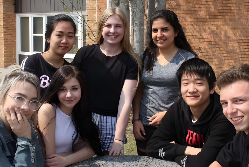 Eine Gruppe von Schülerinnen und Schülern steht vor einem Backsteingebäude auf dem Gelände des Waterloo Region District School Board.