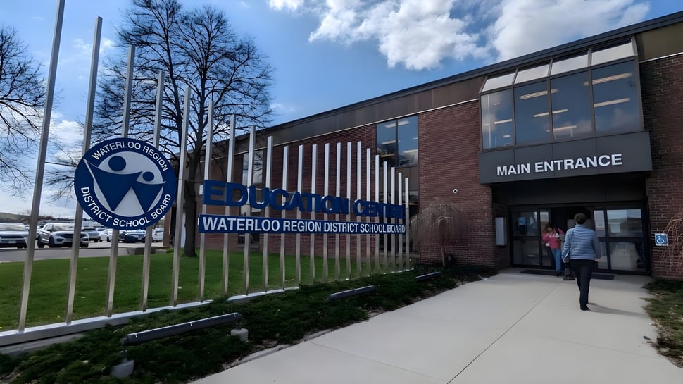 Das Backsteingebäude mit dem Eingang und dem Logo des Waterloo Region District School Board ist von Bäumen und einem gepflasterten Weg umgeben.