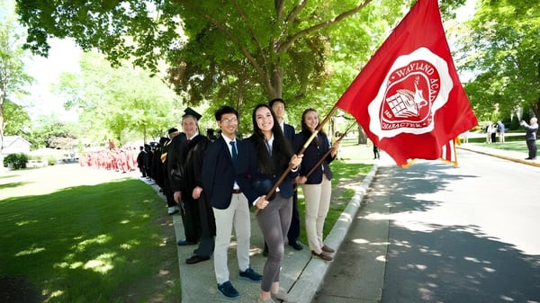 Eine Gruppe von Schülerinnen und Schülern der Wayland Academy hält eine rote Fahne auf einem von Bäumen gesäumten Weg.