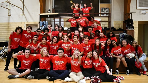 Eine Gruppe von Schülerinnen und Schülern der Wayland Academy in roten T-Shirts versammelt sich in einer Sporthalle.