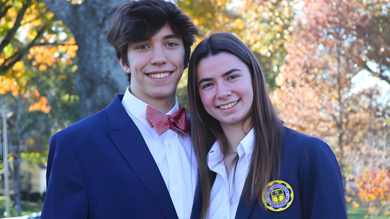 Zwei Schüler der Webb School stehen lächelnd im herbstlichen Außenbereich mit Bäumen im Hintergrund.