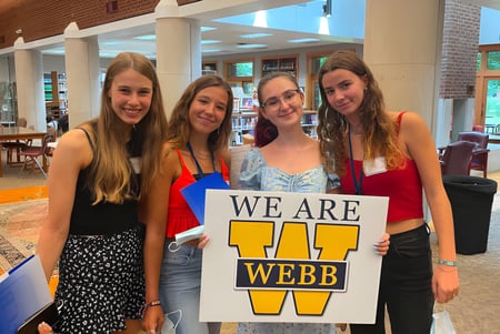 Vier Schülerinnen der Webb School halten gemeinsam ein Schild mit der Aufschrift ‚WE ARE WEBB‘ in einem Café.