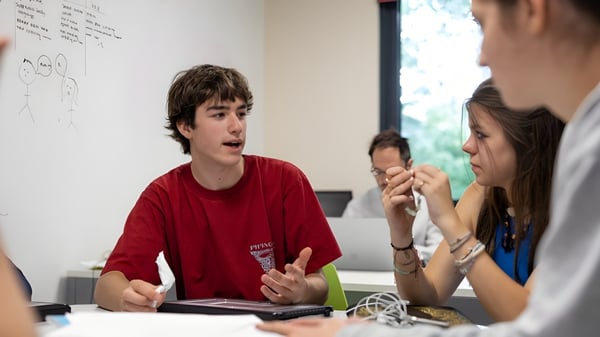 Ein Schüler des Wellington College führt eine Diskussion mit zwei weiteren Personen in einem Klassenraum vor einem Whiteboard.