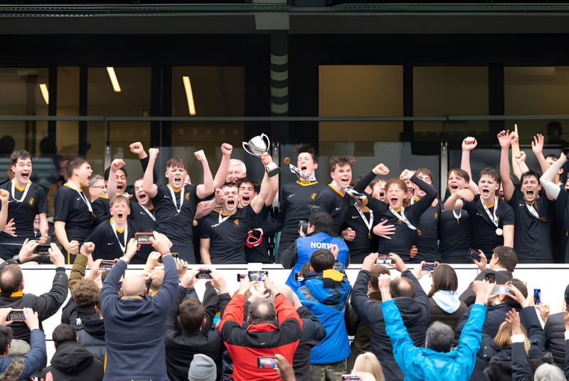 Eine Gruppe von Schülerinnen und Schülern in schwarzen Uniformen feiert gemeinsam auf dem Campus des Wellington College.