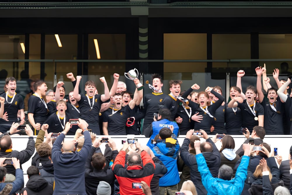 Eine Gruppe von Schülerinnen und Schülern in schwarzen Uniformen feiert gemeinsam auf dem Campus des Wellington College.