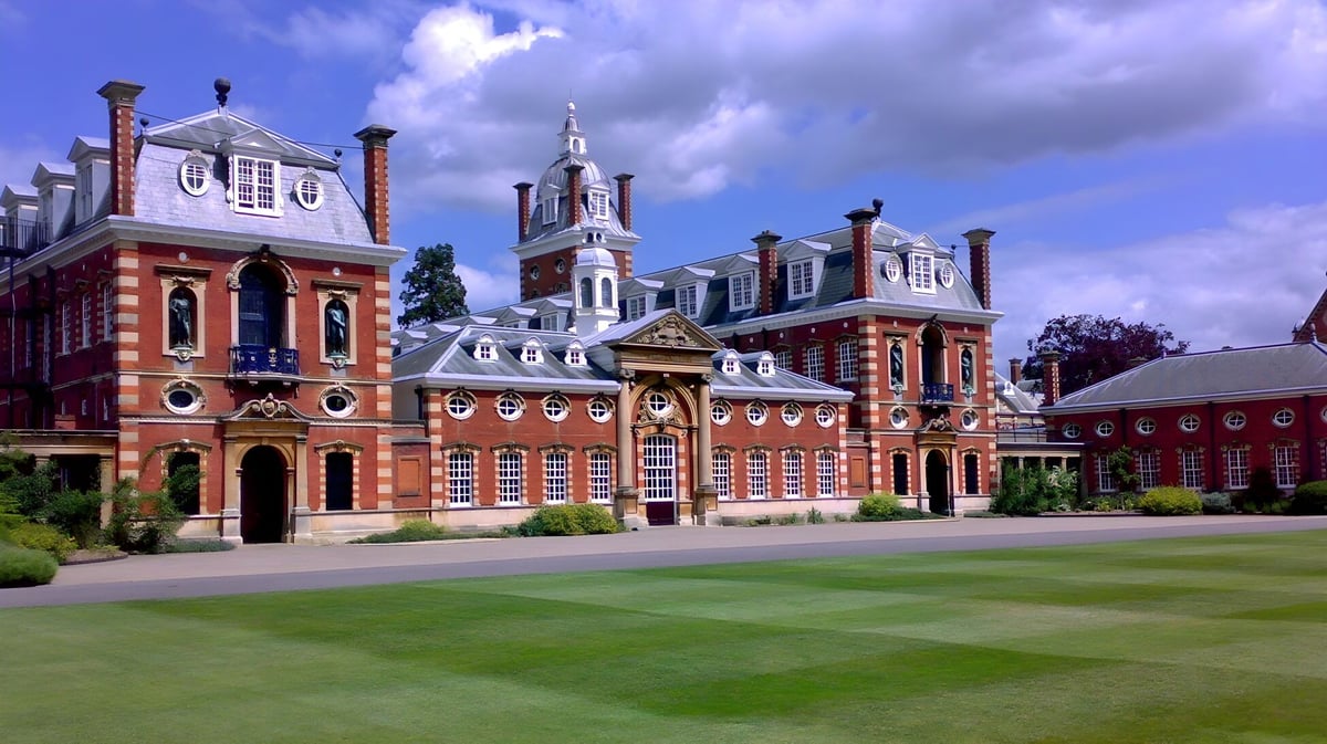 Das Wellington College zeigt ein historisches Backsteingebäude mit einem zentralen Turm und gepflegtem Rasen bei bewölktem Himmel.