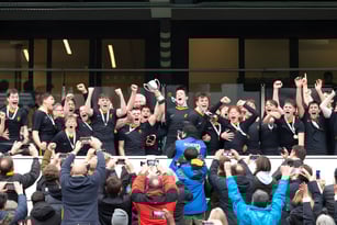 Eine große Gruppe Schüler in schwarzen Uniformen feiern gemeinsam auf dem Campus des Wellington College.