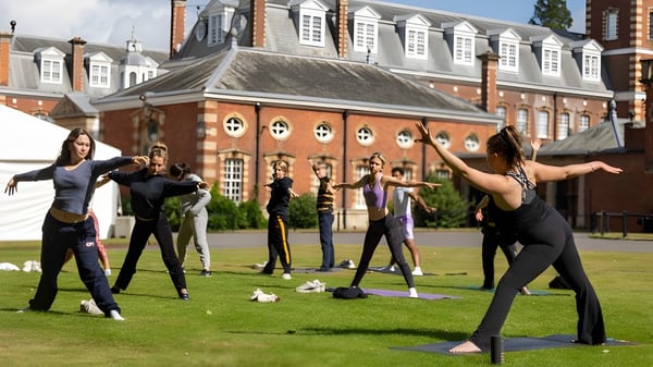 Schülerinnen und Schüler des Wellington College praktizieren Yoga auf einer Rasenfläche vor einem historischen Backsteingebäude.