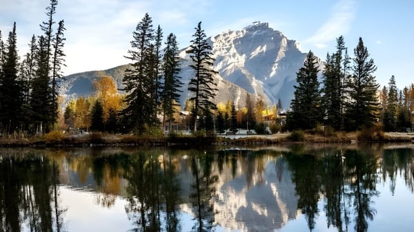 Ein ruhiger Bergsee mit umgebenden Kiefern und einem schneebedeckten Gipfel spiegelnd im Wasser.