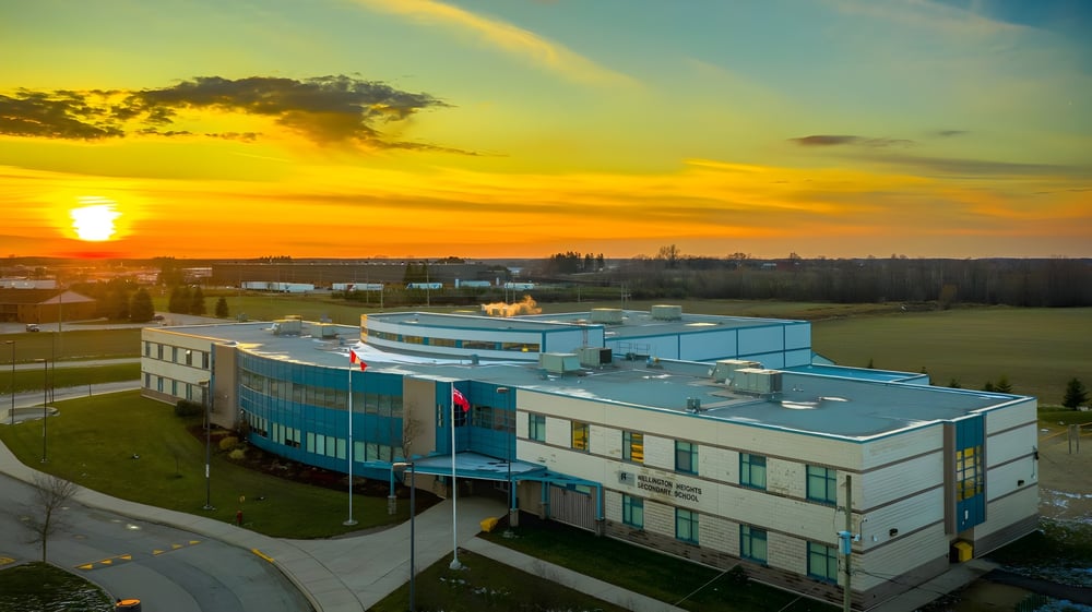Das moderne Gebäude der Wellington Heights Secondary School mit blauer Fassade steht vor einem farbenfrohen Sonnenuntergang.