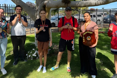 Eine Gruppe von Schülerinnen und Schülern sowie Erwachsenen steht auf einer Wiese auf dem Gelände der Wellington High School vor einem großen Baum.